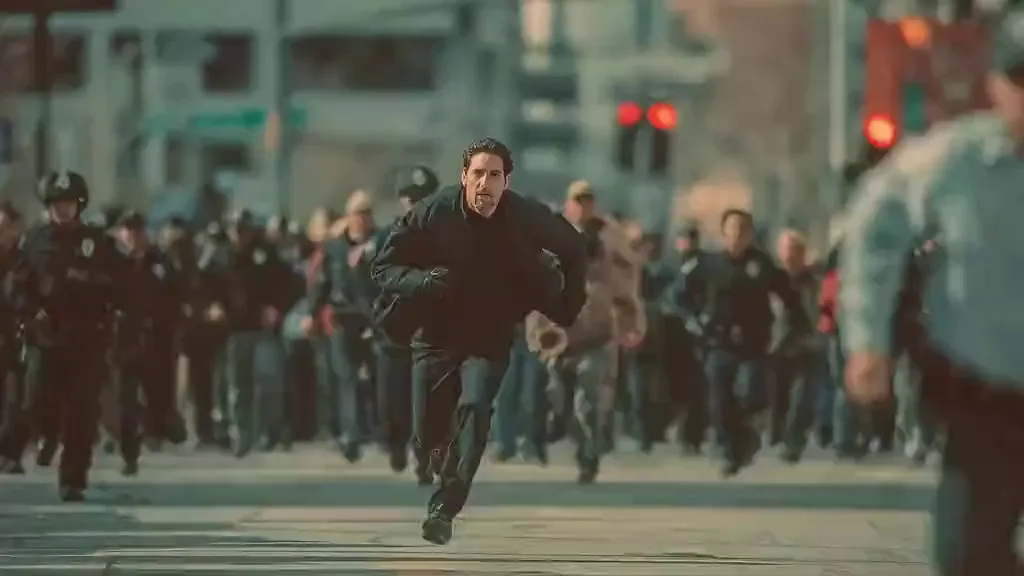 seedance2.0 キャラクターの対話 | カメラは黒衣の男が急速に逃げる様子を追い、群衆が後ろを追う。カメラはサイドトラッキングショットに切り替わり、パニックになった男が道端のフルーツスタンドを倒し、這い上がって走り続ける。混沌とした群衆の音。